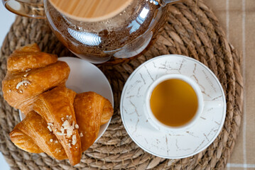  Delicious croissants and cup of tea in warm morning light. Cozy home breakfast concept.