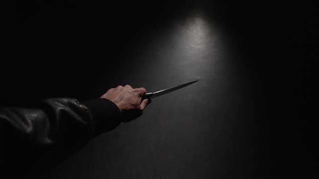 POV, close-up first person view of a man's hand with big knife. Criminal hand holding kitchen knife in threatening posture on dark background, causes alarm and danger.