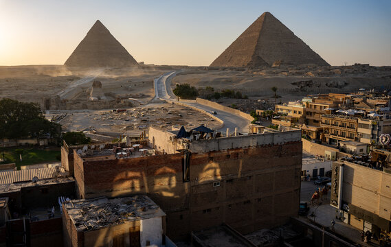 Great pyramid of Giza Im Vordergrund stehen flache Wohnh&auml;user und D&auml;cher, dahinter erheben sich in der W&uuml;ste Pyramiden Cheops-Pyramide , Chephren- im Licht der tief stehenden Sonne.