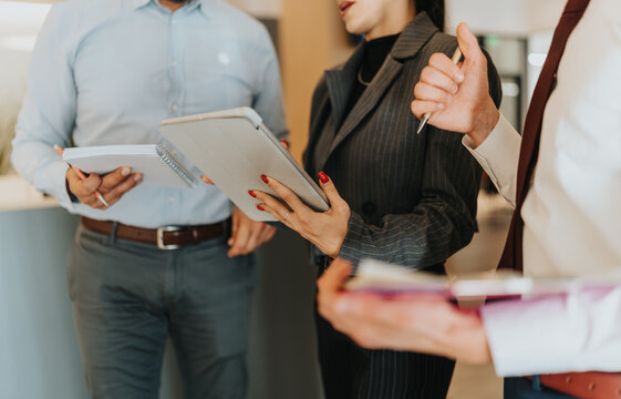 A diverse group of professionals collaborates in a modern office, holding tablets and notebooks while discussing ideas and plans in a business meeting. - Powered by Adobe