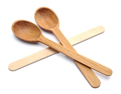 Two wooden spoons rest atop two crossed, light-colored wooden sticks, against a bright white backdrop. The spoons show wood grain