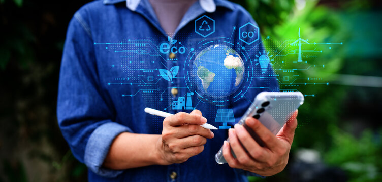 Eco technology and sustainability concept with digital green energy icons surrounding the Earth. Person using smartphone and stylus to support environmental innovation, renewable energy.