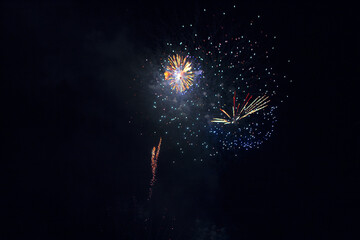 Fireworks exploding against dark night sky. Multiple colorful bursts and streaking light trails illuminate the black background with various patterns of light and smoke
