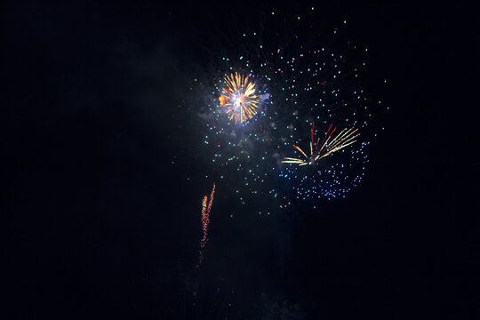 Fireworks exploding against dark night sky. Multiple colorful bursts and streaking light trails illuminate the black background with various patterns of light and smoke