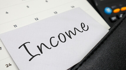 A white envelope with Income written on it, tucked into a calendar alongside a calculator, symbolizing financial concept.
