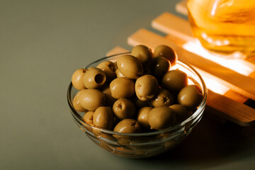 Green olives in a clear bowl next to a warm light source on a flat surface