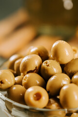 Olives presented in a clear bowl on a wooden surface with a bottle of oil in the background