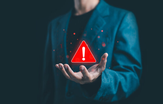 Cybersecurity alert concept showing a businessman holding a glowing red warning sign with an exclamation mark, symbolizing danger, data risk, caution, system error, and digital security awareness.
