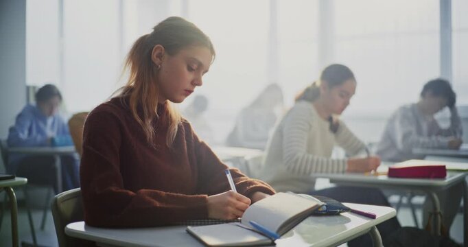 Teenagers Writing Completing Task in Classroom. Diverse Group of Students Sits Desks in Focusing Intently on Writing Assignments. Concept Student Concentration, Academic Workload in Modern Education.