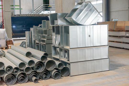 Metal ventilation ducts in an industrial warehouse. Stacks of round and rectangular HVAC ducts ready for installation in building ventilation systems.