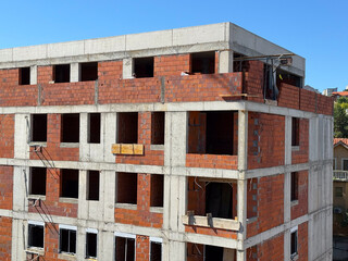 Unfinished brick apartment building under clear blue sky. Urban development, construction progress, and architectural growth.