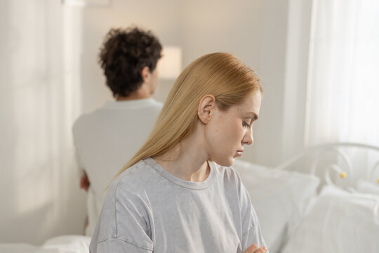 Sad couple sitting on bed facing away from each other, showing emotional distance and relationship conflict. Scene of misunderstanding, tension and lack of communication in romantic relationship.