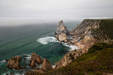 Dramatic coastal cliffs and rock formations at Cabo da Roca, Portugal, with mist rolling over the Atlantic Ocean on a moody day