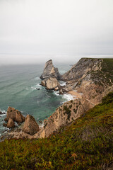 Vertical view of Cabo da Roca's rugged cliffs and turquoise waters beneath low-hanging mist on Portugal's Atlantic coast