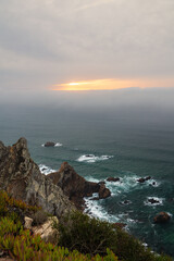 Sunset over the Atlantic Ocean at Cabo da Roca, Portugal with rugged cliffs and crashing waves beneath a foggy sky