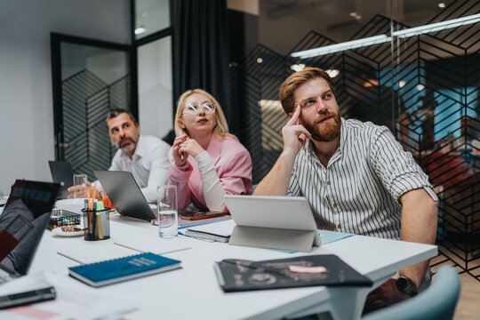 Diverse professionals in a bright office collaborate over laptops and notes during a strategic meeting. - Powered by Adobe