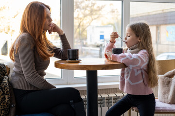 Pretty caucasian mother and her daughter sitting in the cafe and drinking cacao or coffee. Reading and looking at the book. Slow motion of cute young woman with her kid