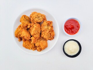 Crispy and crunchy fried chicken in a white plate and mayonnaise sauce in a small black bowl and chili sauce in a small white bowl on a white background.