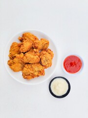 Crispy and crunchy fried chicken in a white plate and mayonnaise sauce in a small black bowl and chili sauce in a small white bowl on a white background.