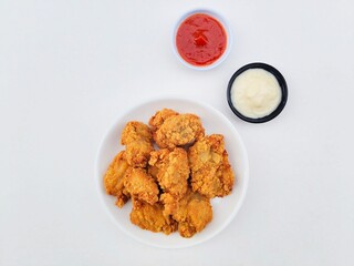 Crispy and crunchy fried chicken in a white plate and mayonnaise sauce in a small black bowl and chili sauce in a small white bowl on a white background.