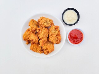 Crispy and crunchy fried chicken in a white plate and mayonnaise sauce in a small black bowl and chili sauce in a small white bowl on a white background.