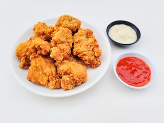 Crispy and crunchy fried chicken in a white plate and mayonnaise sauce in a small black bowl and chili sauce in a small white bowl on a white background.