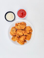 Crispy and crunchy fried chicken in a white plate and mayonnaise sauce in a small black bowl and chili sauce in a small white bowl on a white background.