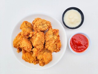 Crispy and crunchy fried chicken in a white plate and mayonnaise sauce in a small black bowl and chili sauce in a small white bowl on a white background.