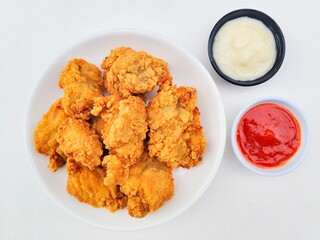 Crispy and crunchy fried chicken in a white plate and mayonnaise sauce in a small black bowl and chili sauce in a small white bowl on a white background.