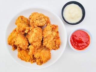 Crispy and crunchy fried chicken in a white plate and mayonnaise sauce in a small black bowl and chili sauce in a small white bowl on a white background.