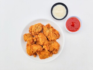 Crispy and crunchy fried chicken in a white plate and mayonnaise sauce in a small black bowl and chili sauce in a small white bowl on a white background.