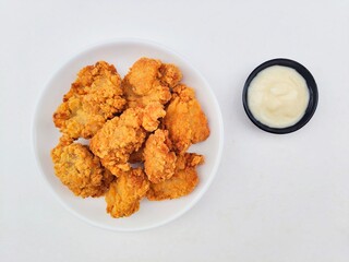Crispy and crunchy fried chicken in a white plate and mayonnaise sauce in a small black bowl on a white background.