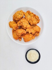 Crispy and crunchy fried chicken in a white plate and mayonnaise sauce in a small black bowl on a white background.
