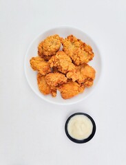 Crispy and crunchy fried chicken in a white plate and mayonnaise sauce in a small black bowl on a white background.