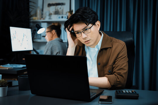 Serious face of thinking businessman focusing laptop to report data analysis social media online project with coworker analyzing stock at back side at over late night time at modern office. Infobahn.