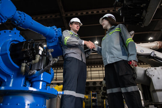 Engineer standing by robotic arm and operating machine in industry factory, technician worker check for repair maintenance electronic operation