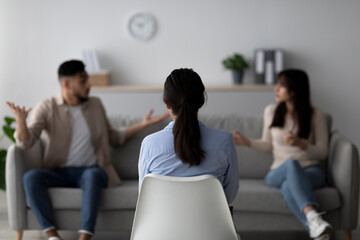 A professional psychologist guides an arab couple through a marital therapy session. The couple expresses concerns while the therapist listens with focus. The setting is a cozy office space.