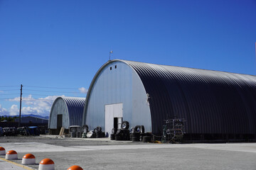 Arched metal hangars on an industrial site. Warehouse, tires and wheels at the entrance, fence...