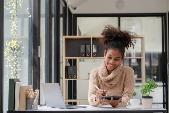 Young African American businesswoman working at a desk and using a digital tablet in the modern office.