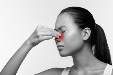 Closeup of a young Japanese woman with closed eyes, rubbing her red sore nose. She appears unhappy...