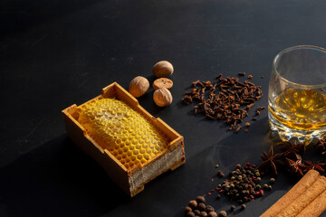 Whiskey and winter spices composition with honeycomb on a dark table. Dramatic overhead shot. Concept of a cozy, spiced alcoholic beverage or gourmet tasting. High-contrast image with deep shadows