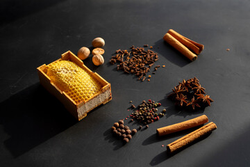 Flat lay composition of aromatic winter spices and natural honeycomb on dark background. Perfect for holiday cooking and baking concepts. Concept of warm beverages, baking ingredients