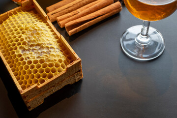 Honeycomb and cinnamon sticks with glass of whiskey on dark background. Minimalist composition. Elegant still life with natural honeycomb, cinnamon, and snifter glass