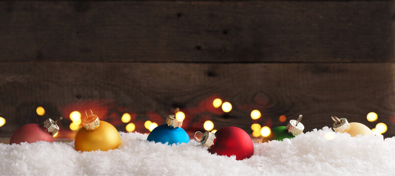 Colorful vintage Christmas baubles in snow on a wooden background with Christmas lights, holiday or seasonal backdrop