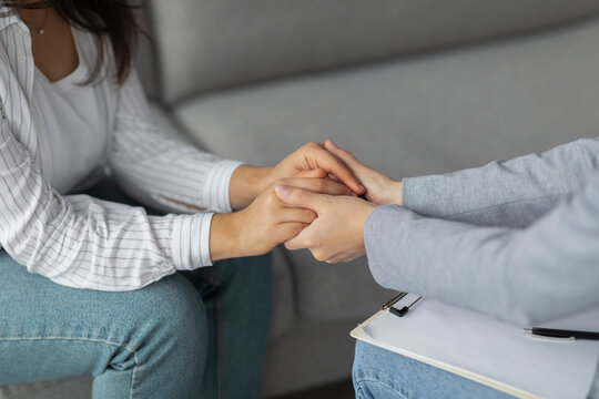 A psychotherapist supports a young woman experiencing depression by holding her hands in a clinic. They are seated together, emphasizing a compassionate connection during a difficult moment.