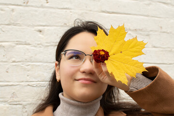 Portrait of a young attractive woman in eyeglasses covering her face with a yellow maple leaf and marigold