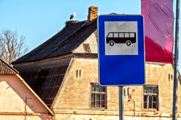 Blank bus stop sign near an old building with a stork resting on the roof in daylight