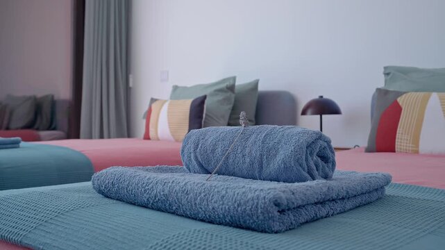 Soft blue towels neatly rolled, resting on teal blanket atop pink bedspread, showcasing pristine hotel room interior with meticulous attention to guest comfort and elegant design