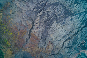 Naklejka premium Drone view of mineral-rich terrain with cracked earth and erosion lines forming organic abstract shapes