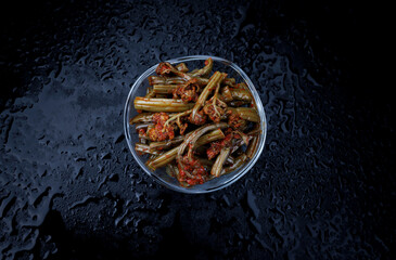 Transparent glass bowl with fern salad with spices on black background. Close-up top view.